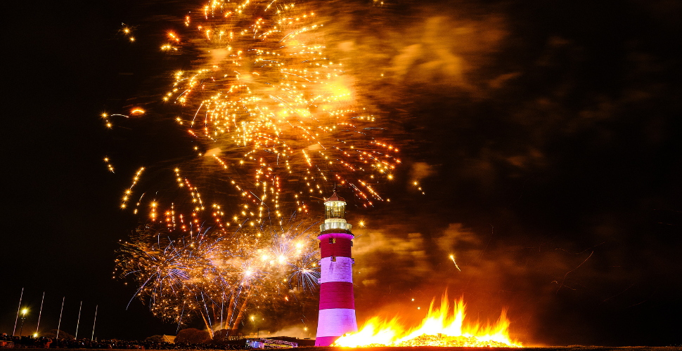 Smeaton's Tower with a bonfire in front of it and fireworks in the night sky behind